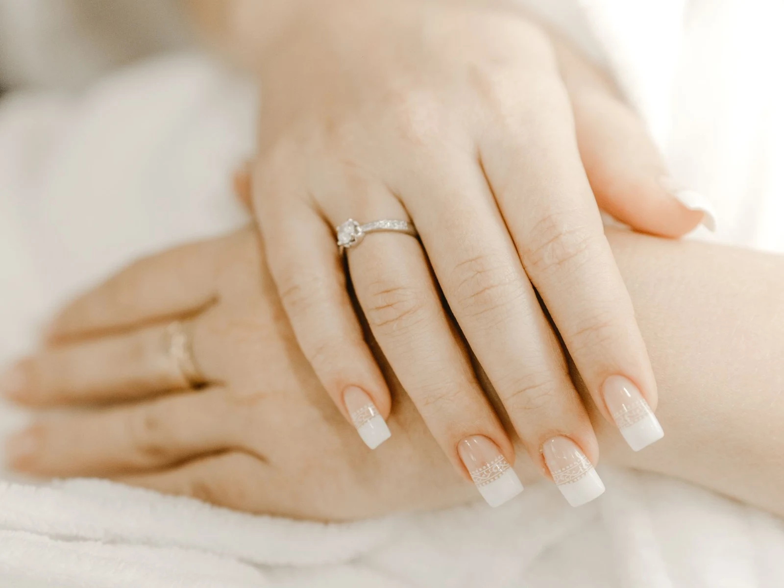 Round solitaire diamond engagement ring on a hand resting on a soft white robe