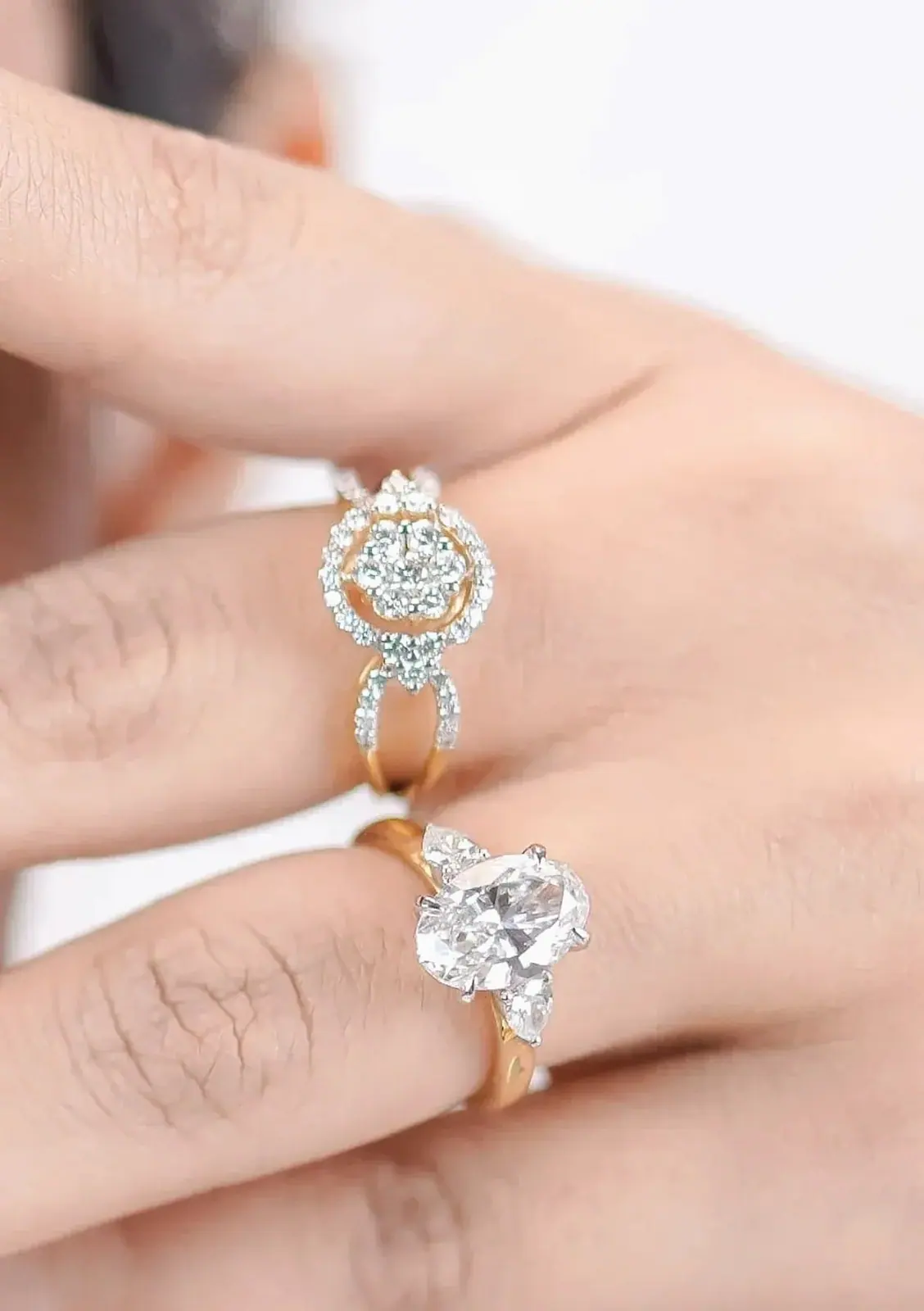 Oval diamond ring with pear side stones beside a diamond cluster ring on the hand