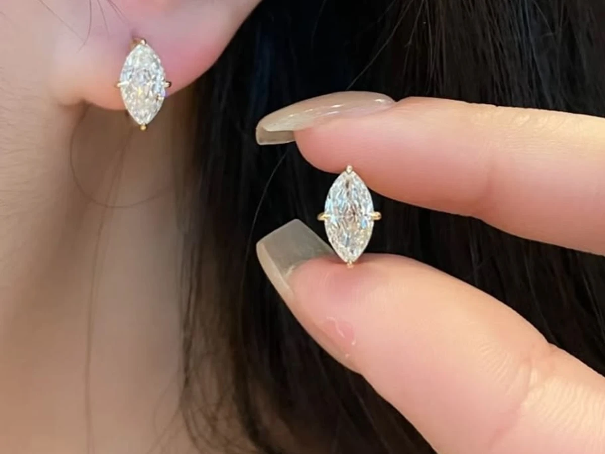Marquise diamond stud earring worn on the ear beside its matching stud held between the fingers
