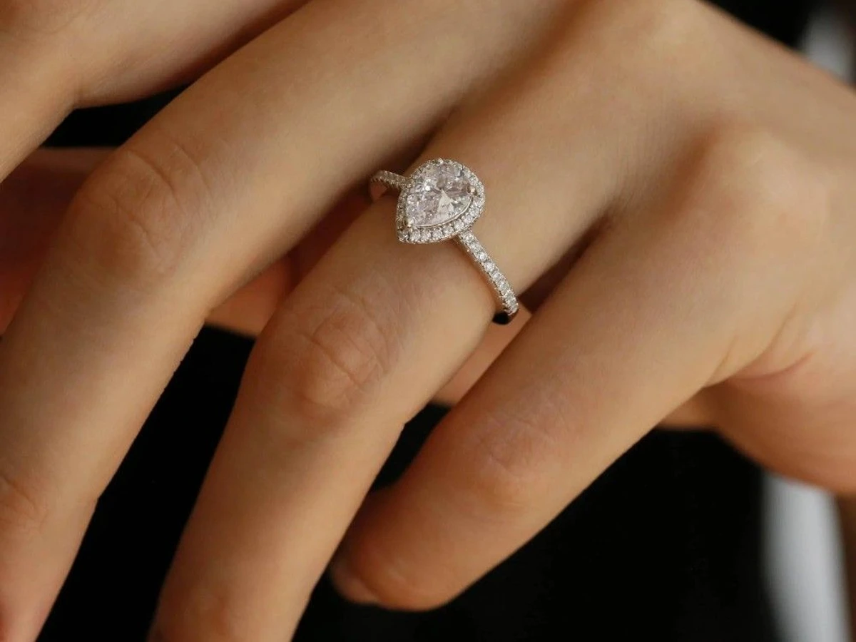 Pear-shaped halo diamond engagement ring with a pavé band in white gold on a hand