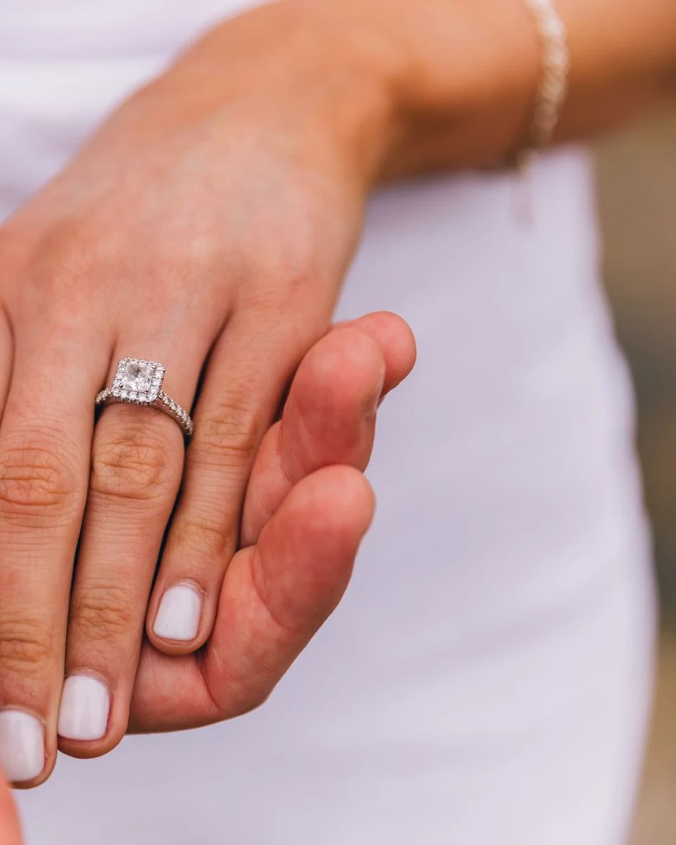 Cushion halo diamond engagement ring on a hand held by a partner