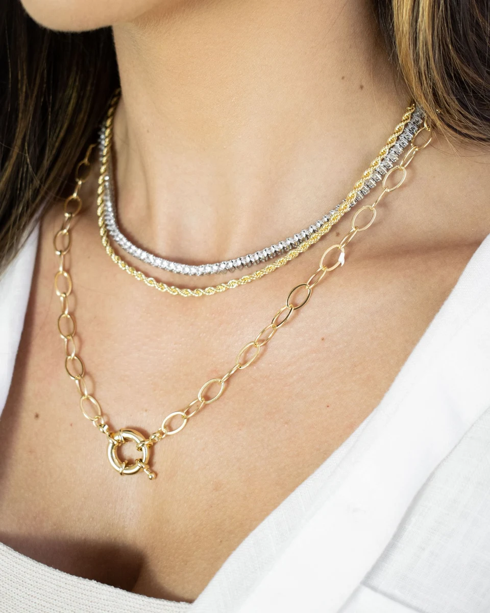 Diamond tennis necklace layered with gold chains over a white shirt