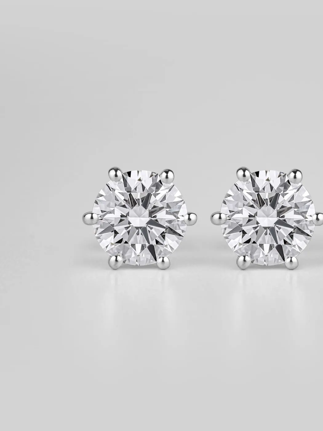 Pair of six-prong round brilliant diamond stud earrings in white gold on pale grey