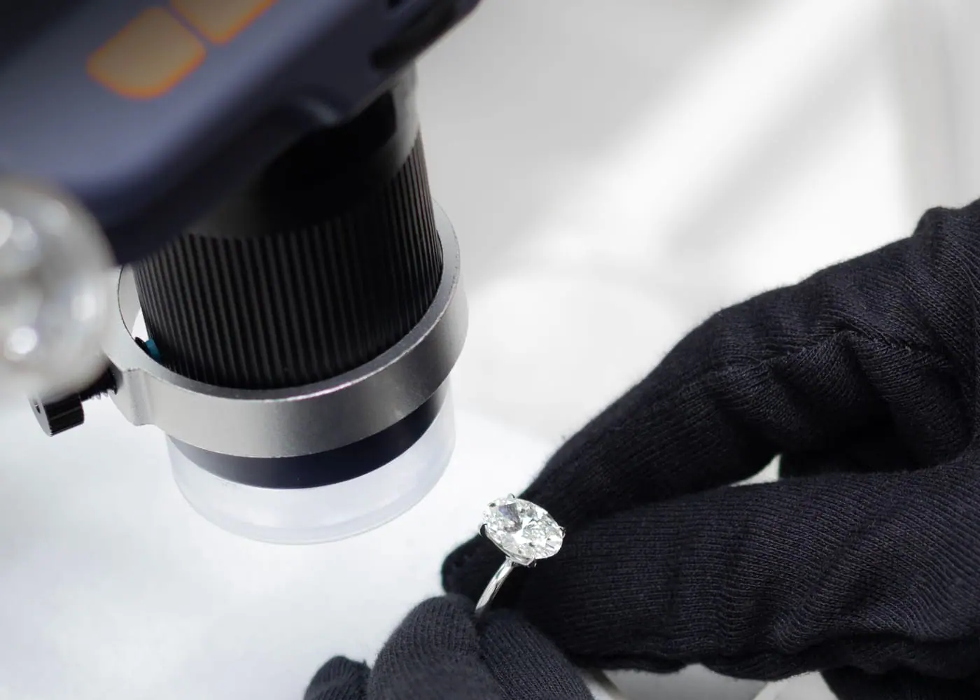 Gloved hands inspecting an oval diamond solitaire ring under magnification