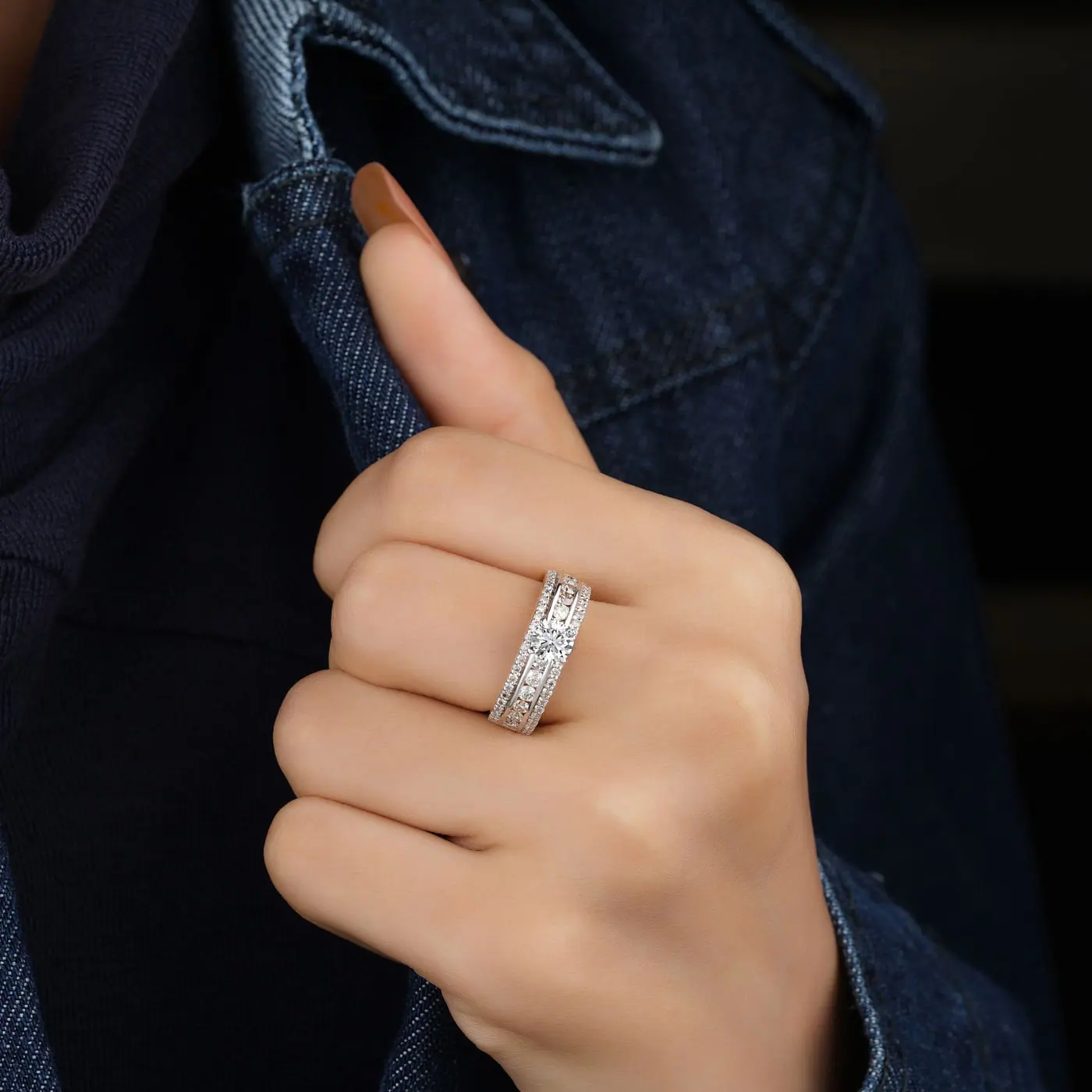 Hand wearing a wide pavé diamond band against a denim jacket