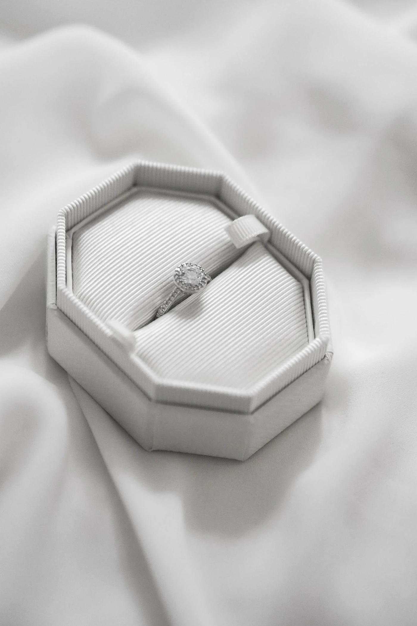 Solitaire diamond ring in an open white octagonal ring box on soft white fabric