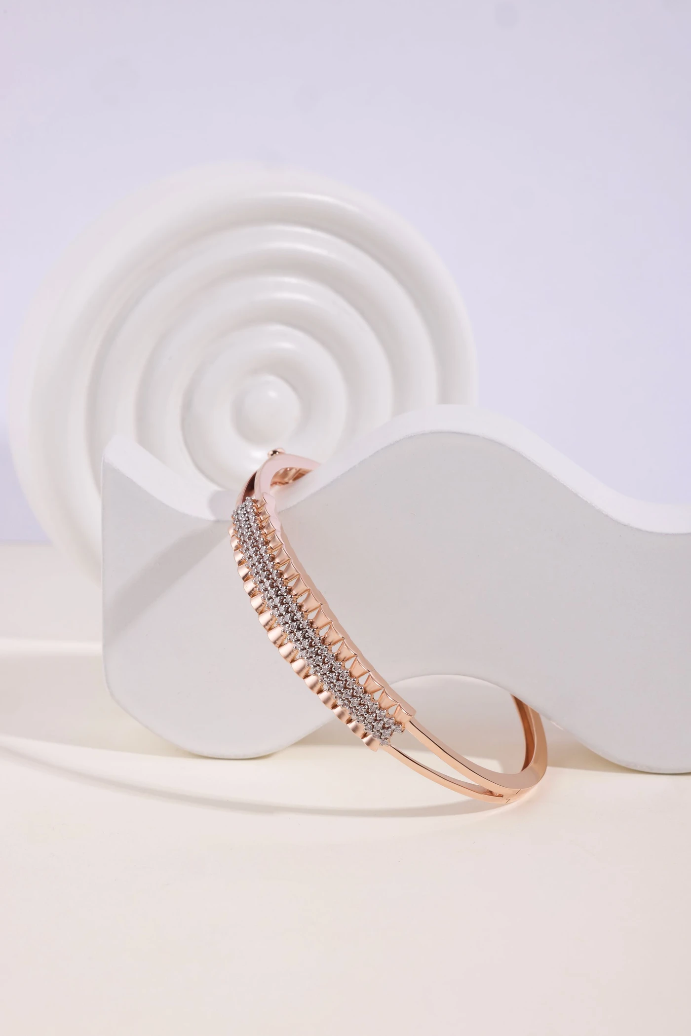 Open diamond bangle with a pavé center row resting against a white sculpted stand
