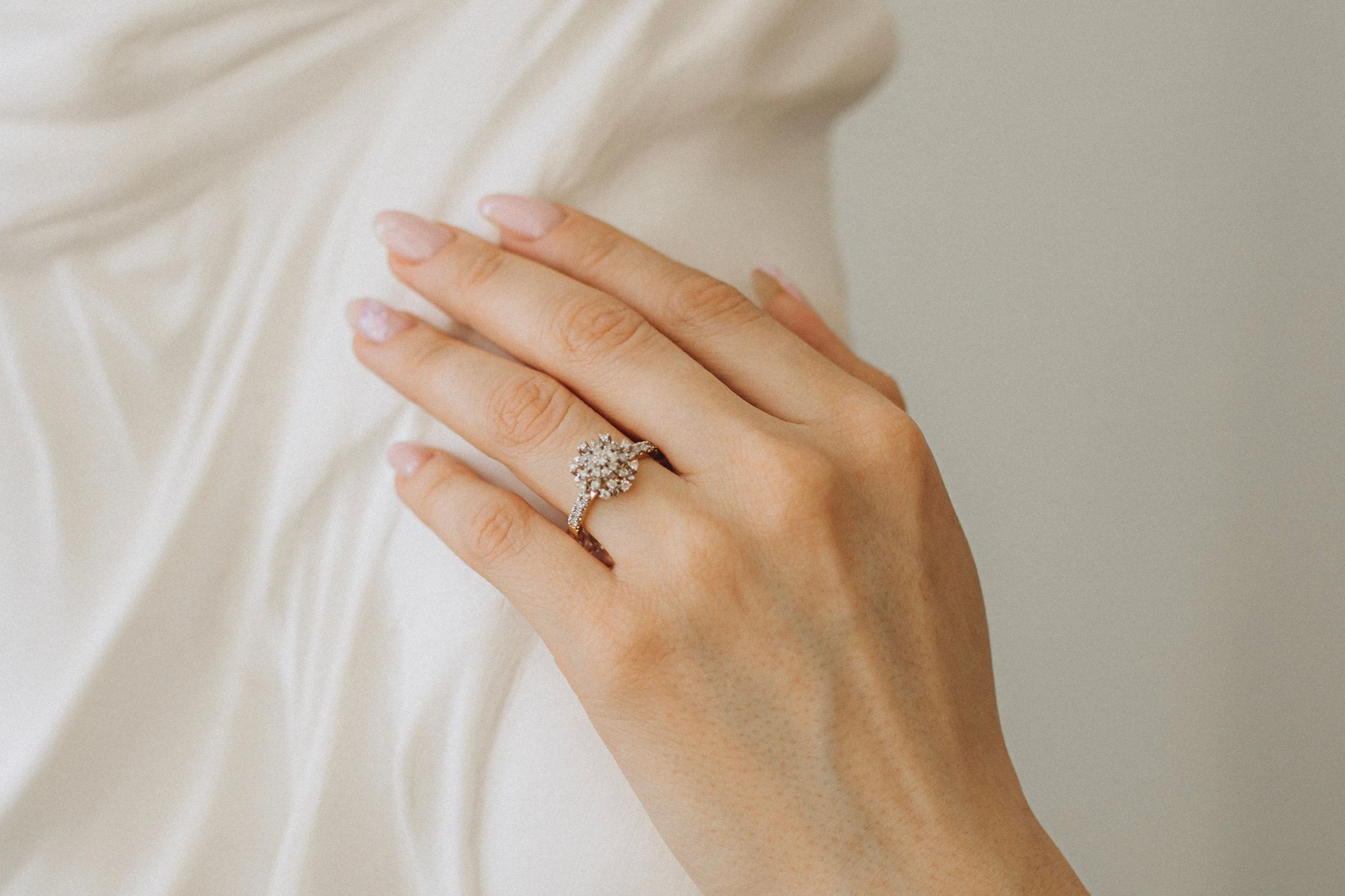 Diamond cluster engagement ring on a hand resting against a white plaster sculpture