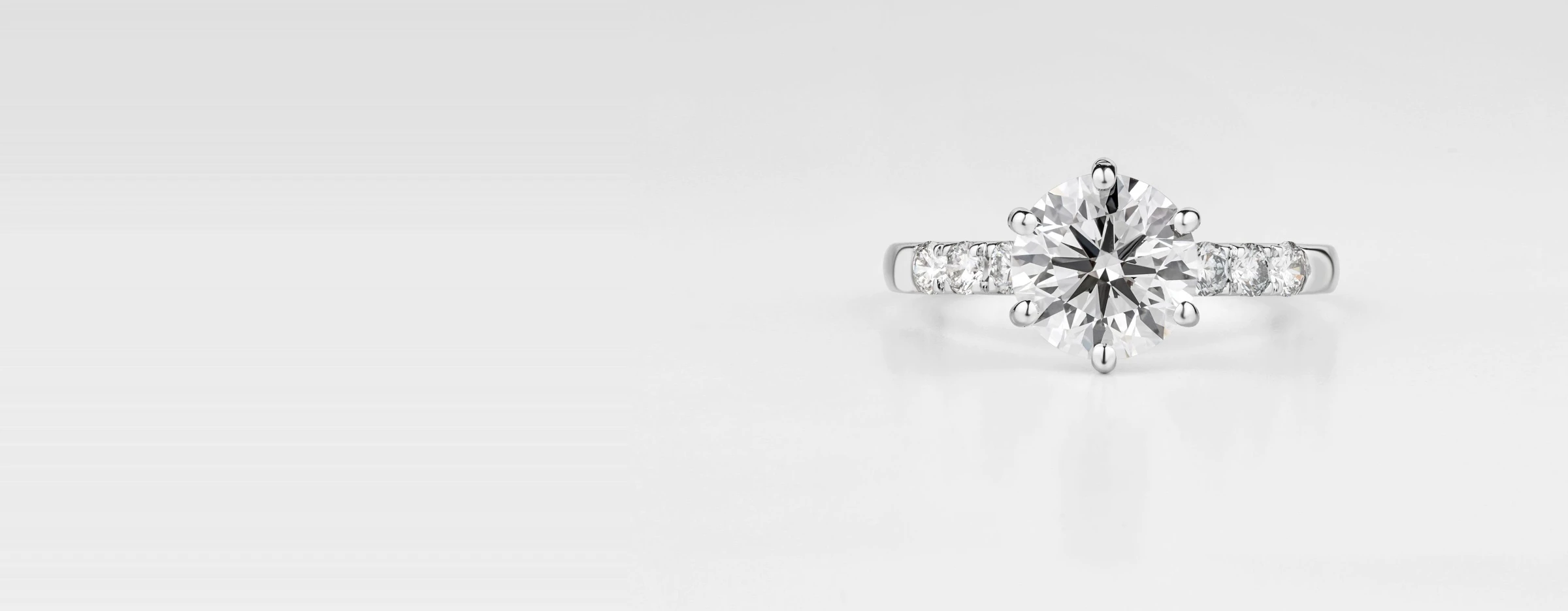 Round brilliant solitaire diamond ring with a pavé band on a light gray backdrop