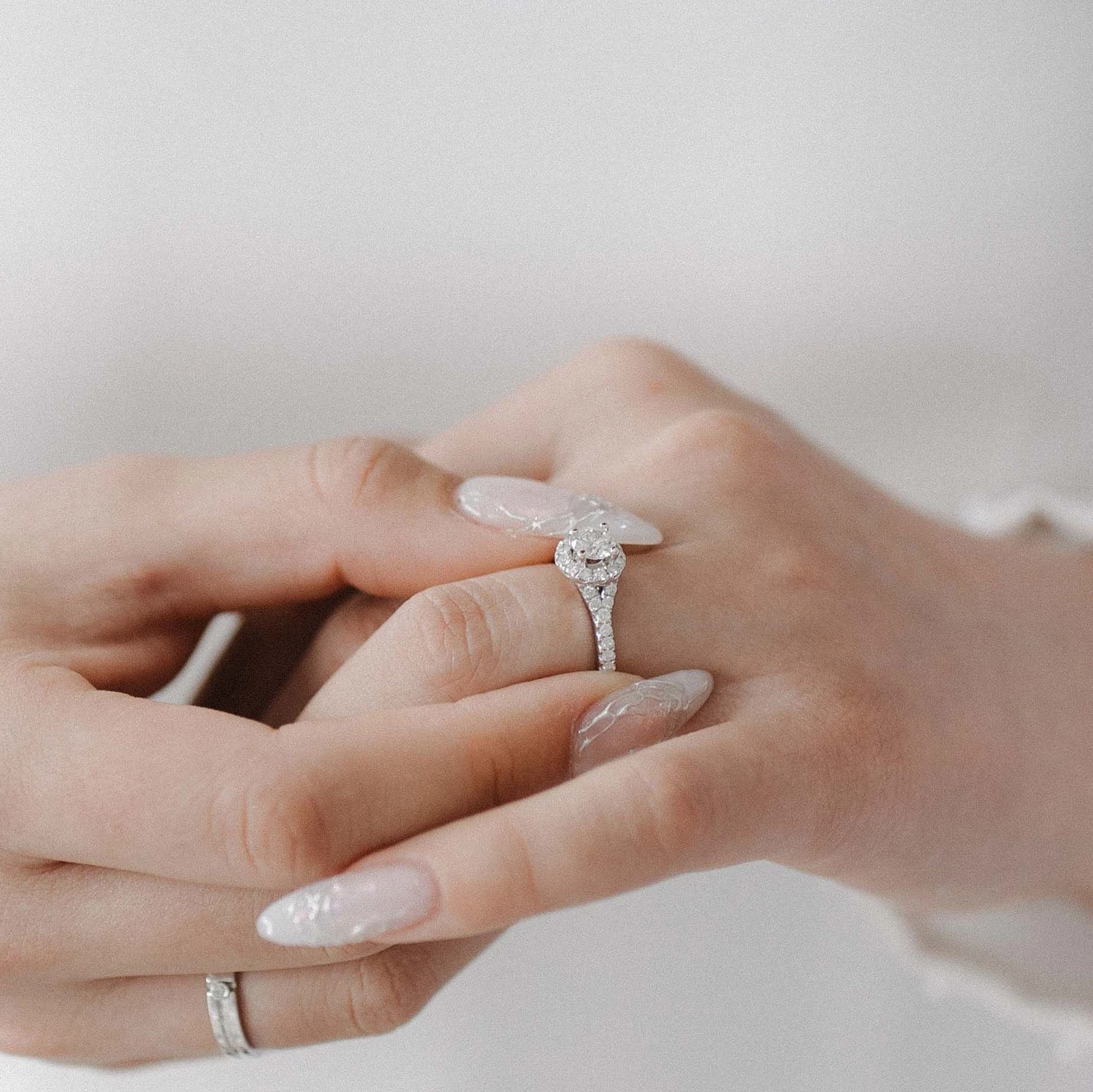 Hands showing a round halo diamond engagement ring with a pavé band