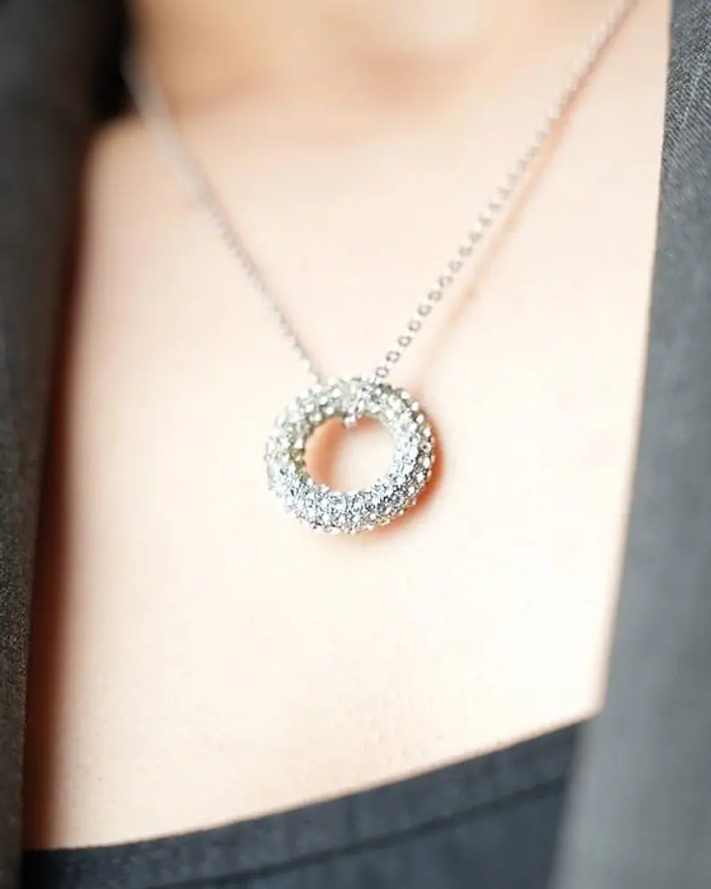 Pavé diamond circle pendant worn with a gray blazer