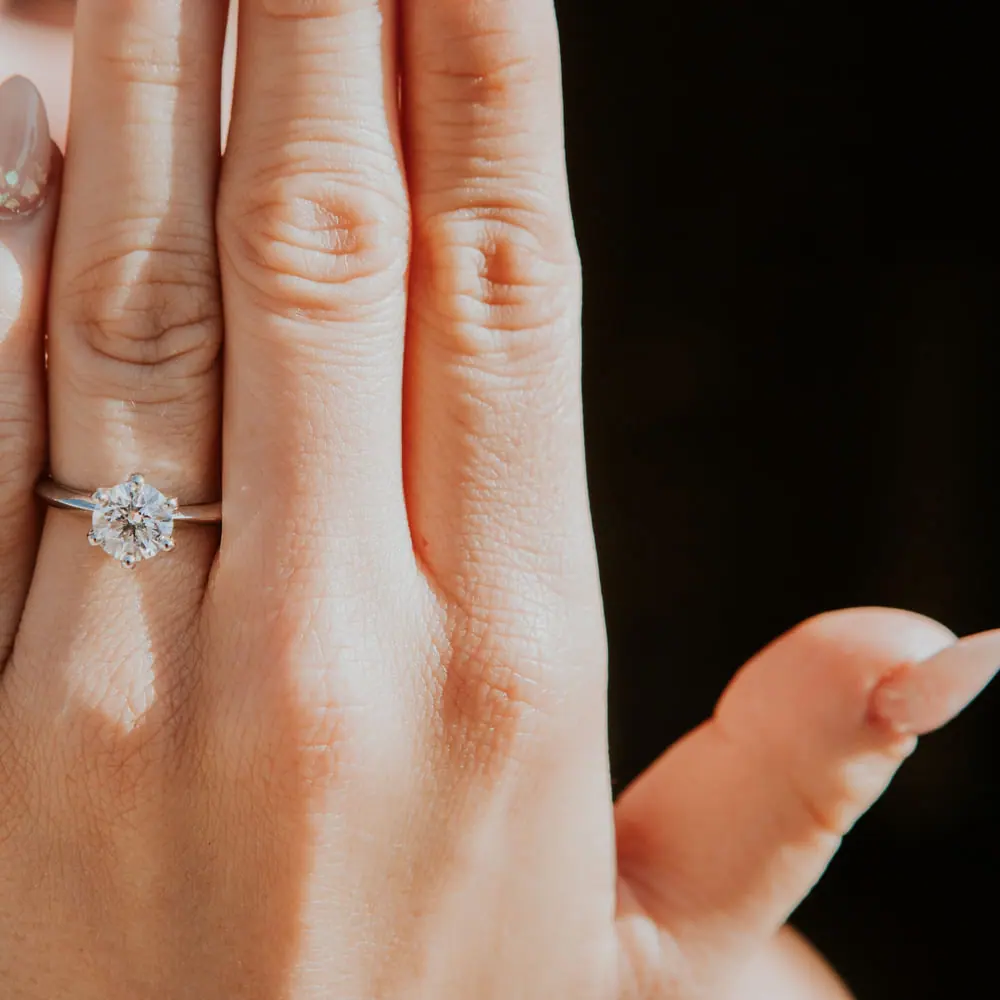 Hand wearing a round diamond solitaire engagement ring in white gold