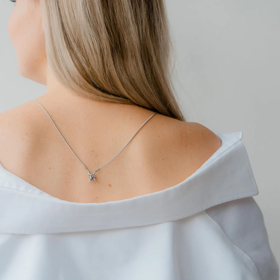 Fine white-gold necklace with a small diamond pendant worn at the back of the neck