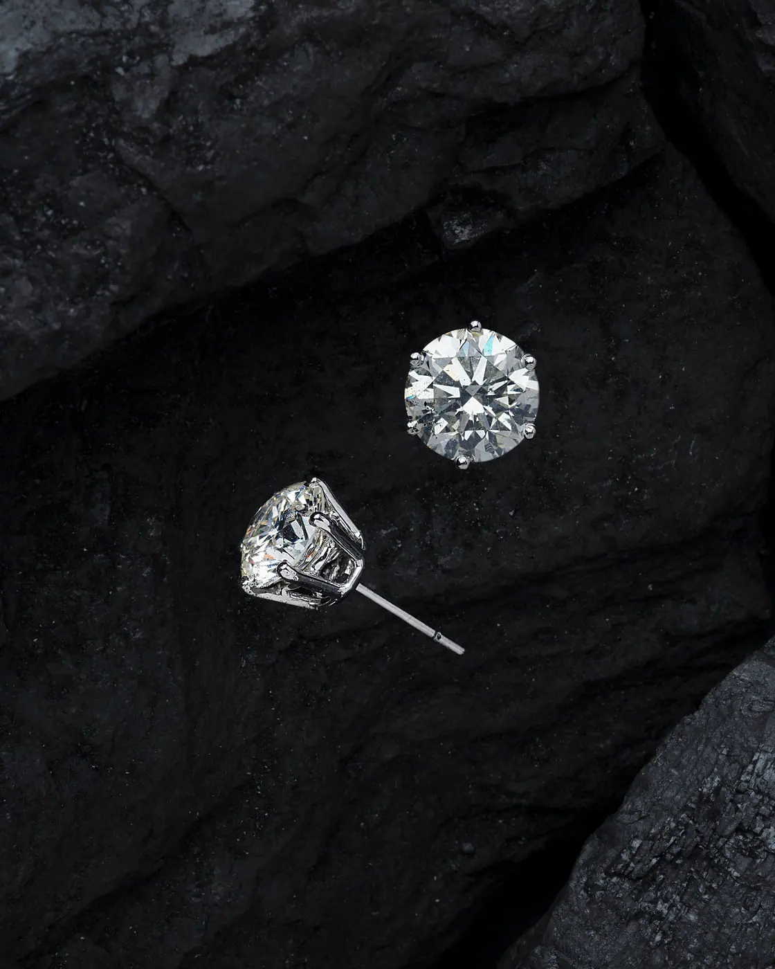 Round diamond solitaire studs resting on dark stone