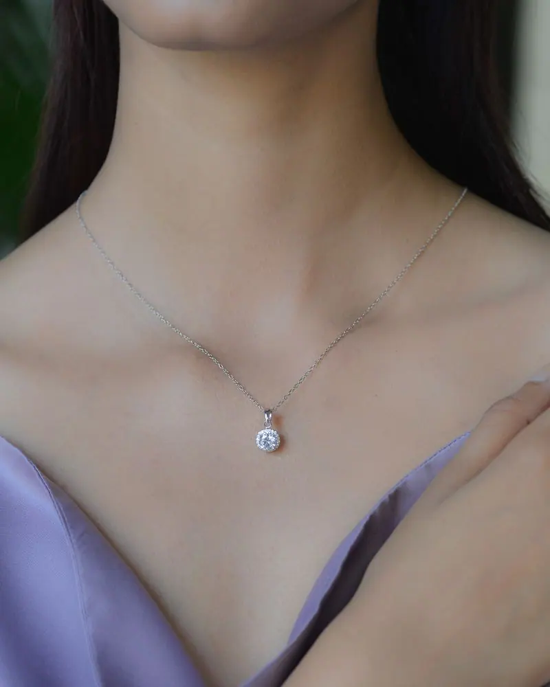 Woman’s neck wearing a white-gold diamond solitaire drop pendant necklace