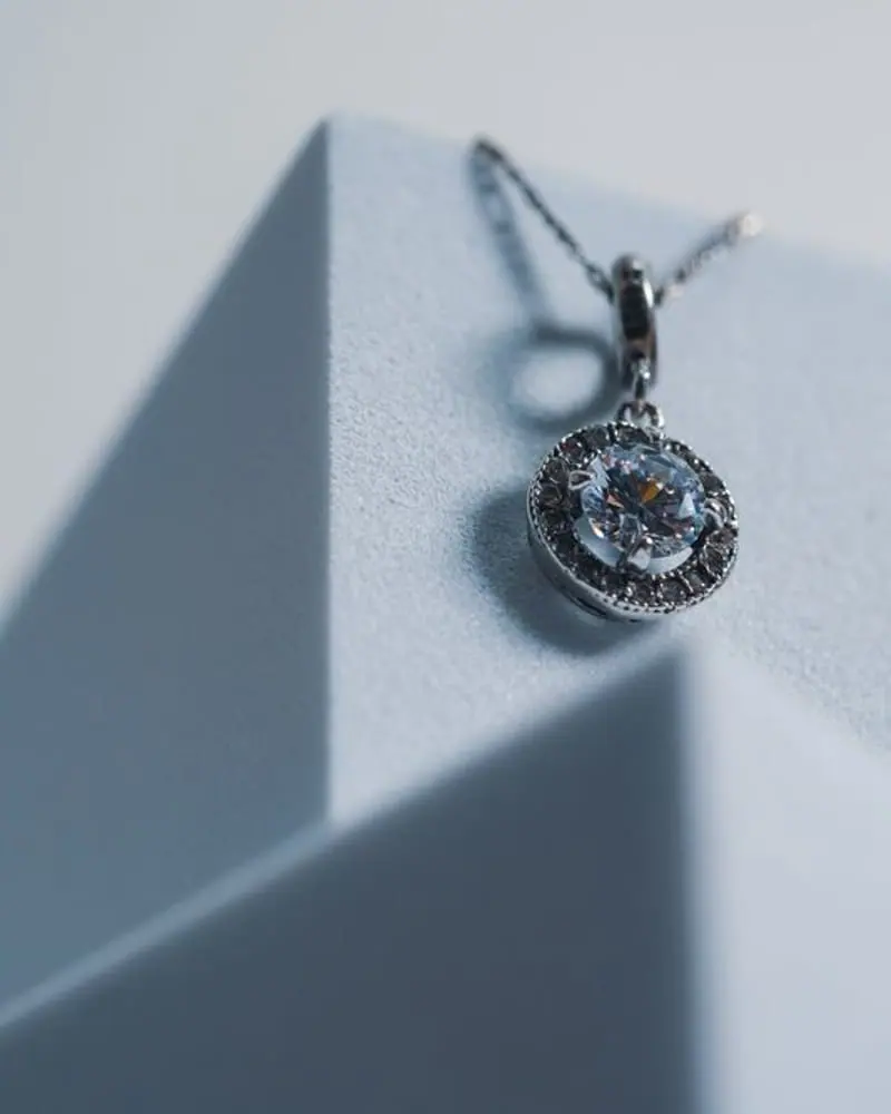 Round halo solitaire pendant on a white step