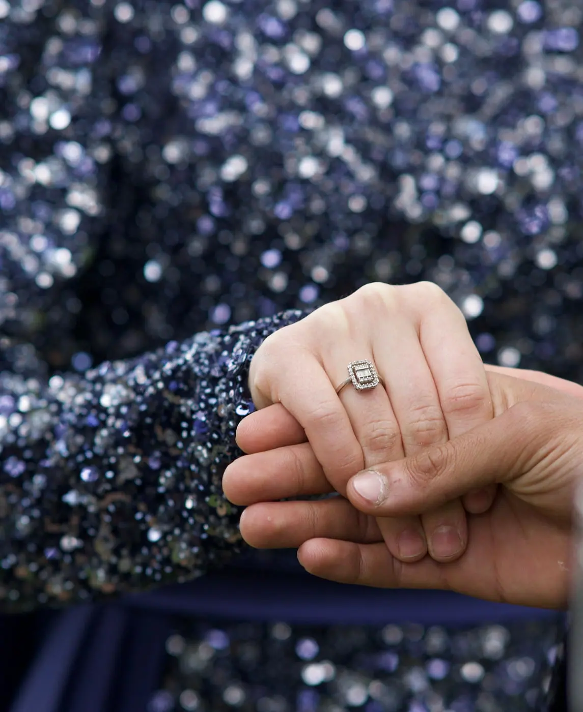 A couple holding hands with a diamond engagement ring