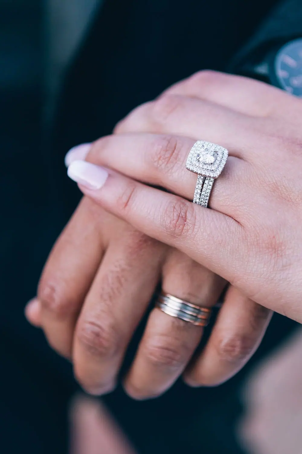 Hands with a cushion halo diamond engagement ring and wedding bands